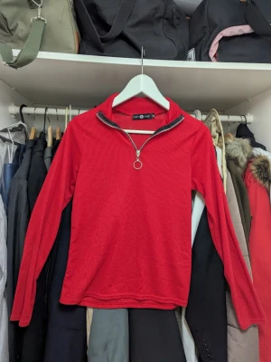Röd ribbad polotopp från Daisy Street - Röd långärmad polotopp från Daisy Street med ribbad struktur och en snygg silverfärgad half zip-dragkedja framtill. Perfekt för dig som gillar en sportig och trendig look. Materialet är mjukt och stretchigt för extra komfort.