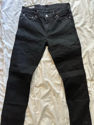 Svarta Levis  jeans  - Säljer ett par svarta jeans från Levis med klassisk femficksdesign och raka ben. Jeansen har knappgylf och silverfärgade nitar. Perfekta för en stilren och enkel look. Storlek: 29:30