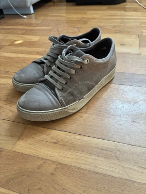 Gråa sneakers från Lanvin - Snygga gråa sneakers från Lanvin med klassisk låg profil. Skorna har ovandel i mocka och tåparti i läder, samt matchande grå skosnören. Yttersulan är vit med diskret struktur och Lanvin-logga undertill. Perfekta för en stilren och avslappnad look. PRIS KAN DISKUTERAS 