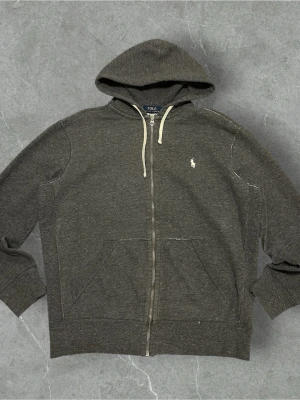 Mörkgrå zip hoodie från Polo Ralph Lauren - 📍Storlek:M  💪🏽Skick:Ny utan prislapp   📐Mått:Längd:58:cm:Bred:50:cm:  📎Material:86%Bomull:14%polyester  📦Skickar alltid inom 48h  ✅Äkthetsgaranti   