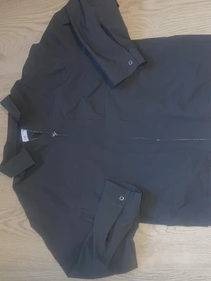 Svart vindjacka från Zara - Stilren svart vindjacka från Zara med dragkedja framtill och två bröstfickor. Jackan har klassisk krage och långa ärmar med tryckknapp vid ärmslut. Perfekt för dig som vill ha en enkel och snygg jacka till vardags.
