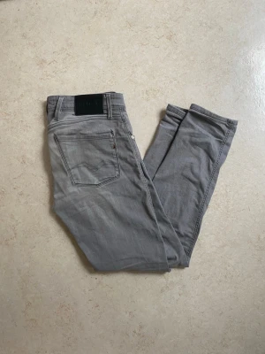Replay anbass jeans - Snygga grå jeans från Replay med klassisk femficksdesign och diskret logga på bakfickan. Jeansen har raka ben och är tillverkade i mjukt denimtyg som ger en avslappnad look. Perfekta för dig som gillar stilrena och tidlösa plagg. Längd 32