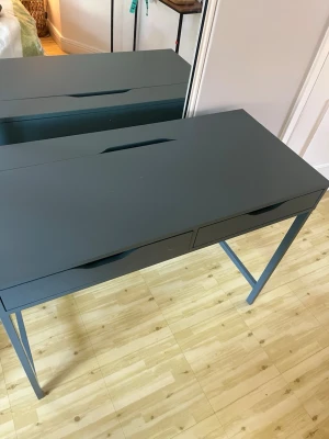 Grått skrivbord med två lådor - Stilrent skrivbord i grön/blå  färg med två praktiska lådor och minimalistisk design. Bordet har raka ben och integrerade handtag för en modern look. Perfekt för plugget eller hemmakontoret. Tillverkat i trä och metall.