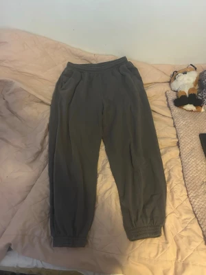 Mörkgrå mjukisbyxor med resår - Mysiga grå mjukisbyxor med resår i midjan och vid bensluten. Byxorna har två sidofickor och är tillverkade i ett mjukt bomullsliknande material. Perfekta för chill dagar hemma eller när du vill vara extra bekväm.