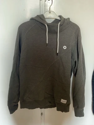 Olivgrön hoodie från Jack and Jones - Olivgrön hoodie från Jack and Jones med vit logga på bröstet och matchande dragsko i huvan. Hoodien har ribbade muddar och en avslappnad passform. Tillverkad i mjukt bomullsmaterial, perfekt för en chill och stilren look. Storlek S, Pris kan diskuteras vid snabb affär!