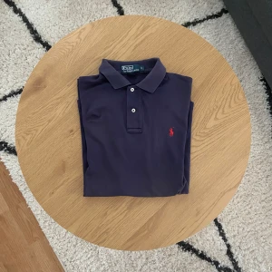 Mörkblå Ralph Lauren Piké - Tjena👋 Säljer denna marinblåa RL Pikén i stretch och mjukt bomullsmaterial. Perfekt för en stilren och tidlös look⏳ Pikén har vit knappslå och röd broderad logga på bröstet!  Pikén är i storlek S men är stor i storlek så passar mer M👕 