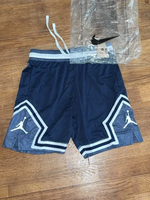 Marinblå Jordan shorts med snörning - Säljer ett par marinblå Jordan shorts med vita detaljer och snörning i midjan. Shortsen har meshmaterial för extra ventilation och den klassiska Jumpman-loggan på båda benen. Perfekta för sport eller chill.