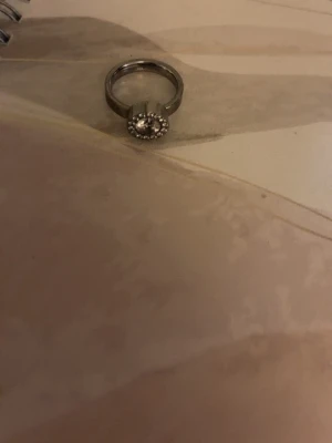 Silverfärgad ring med glittrande stenar - Säljer en snygg silverfärgad ring från Edblad med rund form och en större glittrande sten i mitten, omgiven av mindre stenar som ger extra bling. Perfekt för dig som gillar stilrena och eleganta smycken.  Köpt för 449kr men den är inte använd någonting alls helt ny utan prislapp box med kommer ej pris går att diskutera 🥰ringen är i storlek 16,1mm 