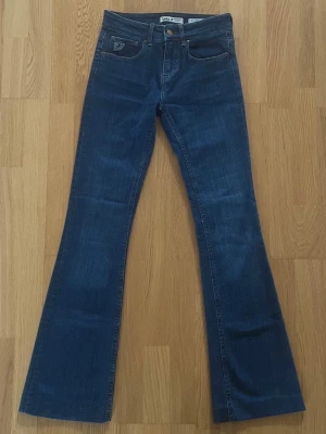 Blå Lois jeans - Storlek: W26 / L32 - Ett par snygga och trendiga Lois jeans i blå denim färg! Modellen Melrose Mid High Flare ger en smickrande passform med utsvängda ben - perfekt både till vardag och fest! Storlek: W26 / L32. Knäpps med knapp och dragkedja. Fickor: Två framfickor och två bakfickor. Material: Bomull, Polyester och Elastan. Tillverkade i Spanien. Säljs i oanvänt skick! Kika gärna in på mina andra annonser, jag säljer flera klädesplagg just nu!