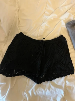 Svarta virkade shorts med snörning - Svarta virkade shorts med snyggt mönster och snörning i midjan. De har en scallop-detalj längst ner och är perfekta för varma dagar. 