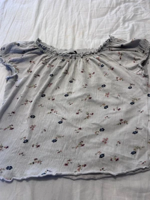 Blommig blus från 157 - Supersöt blommig blus från 157 med små rosa och blå blommor. Blusen har korta ärmar, rynkad halsringning och ett luftigt, flowy tyg som känns perfekt för varmare dagar.