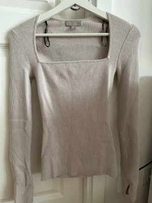 Beige stickad topp med fyrkantig urringning - Beige stickad topp från h&m med ribbad struktur och snygg fyrkantig urringning. Figurnära passform och stretchigt material som ger en clean och modern look. Perfekt att styla med jeans eller kjol för en cool vibe.