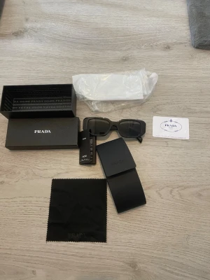 Svarta solglasögon  - Snygga svarta solglasögon från  med rektangulära bågar. Kommer med originalfodral, putsduk, certifikat och låda. Perfekta för dig som vill ha en stilren och exklusiv accessoar till sommaren.