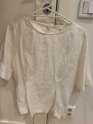 Vit linnetopp med halvärm - En stilren vit linnetopp med rund halsringning och halvärm. Toppen har en enkel och avslappnad passform, perfekt för en fräsch look. Materialet är lätt och andas, vilket gör den skön att bära under varmare dagar.