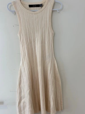 Ribbad ärmlös klänning från vero moda - Superfin ärmlös klänning från vero moda i ribbad beige stickad bomull. Klänningen har rund halsringning och en lätt utställd passform som ger en avslappnad men ändå stilren look. Perfekt för varmare dagar och enkel att styla med accessoarer.