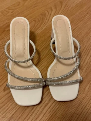 Vit silver klackar sandalett strass glitter - Vita klackar med tre glittrande silvriga strassband över foten.