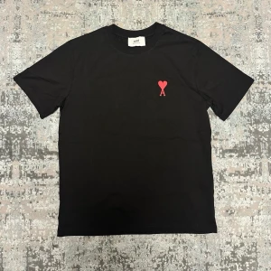 Svart t-shirt - Svart t-shirt med röd broderad logga i form av ett hjärta och bokstaven A på bröstet. Klassisk passform med korta ärmar och rund halsringning. Perfekt för en stilren och trendig look.