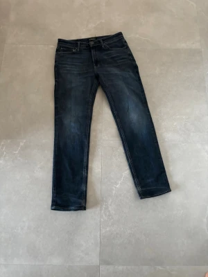 Mörkblå Jack&Jones  - Snygga mörkblå regular fit jeans med klassisk femficksdesign och lätt slitna detaljer. Jeansen har normal midja och raka ben, perfekta för en avslappnad och trendig look. Tillverkade i denim med stretch för extra komfort.