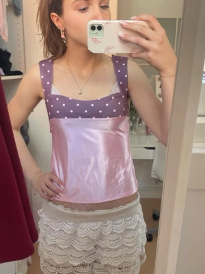 Rosa och lila prickig linnetopp - Söt linnetopp i glansigt rosa tyg med lila partier upptill och axelband, dekorerad med vita prickar. Toppen har breda axelband och är ärmlös, perfekt för en trendig och lekfull look.
