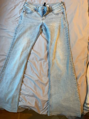 Ljusblå utsvängda jeans - Snygga ljusblå jeans med utsvängda ben och klassisk femficksdesign. Jeansen har hög midja och är tillverkade i denim med en lätt tvättad look. Perfekta för dig som gillar retrostil och vill sticka ut med en cool siluett.