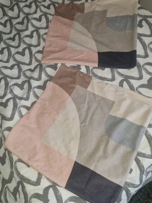 Kuddfodral  - Två kuddfodral i bomull med geometriskt mönster i beige, rosa, grått, brunt och svart i mjukt och lent material. Fodralen har en modern design med olika färgblock och passar perfekt för att ge soffan eller sängen en stilren touch. Måtten är ca 47.5×49.5cm