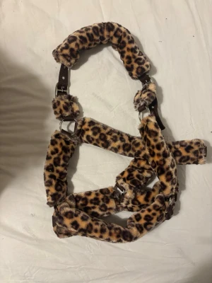 Leopardmönstrad grimma till häst - Säljer en grimma till häst med mjuk, fluffig leopardmönstrad fuskpäls. Grimman har metallspännen och justerbara remmar i brunt tyg. Storlek Full och använd en gång. 