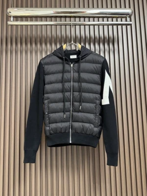 Moncler cardigan - Säljer en svart pufferjacka från Moncler med stickade ärmar och huva. Jackan har dragkedja framtill, quiltad kropp och ett stort vitt märke på ena ärmen. Perfekt för dig som vill ha en sportig och trendig look.
