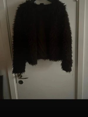 Svart fluffig pälsjacka - Säljer en svart, kort och superfluffig pälsjacka med lång ärm. Jackan har en oversized look och är gjord i fuskpäls som ger en riktigt mjuk och trendig känsla. Perfekt för dig som vill sticka ut och hålla dig varm under kalla dagar.