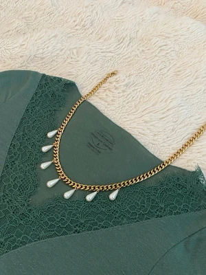 Guldfärgat halsband med pärldroppar - Snyggt halsband i guldfärgad rostfritt med kedja och droppformade vita pärlor som hänger längs framsidan. Perfekt accessoar för att lyfta din outfit med en elegant touch. Passar till många olika stilar och är lätt att matcha.