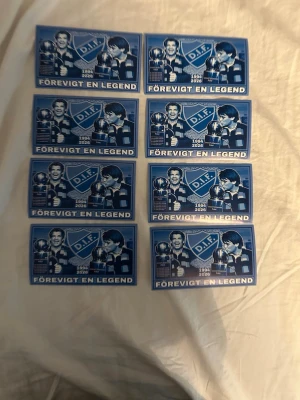 DIF klistermärken 'Förevigt en legend' - Säljer åtta blåa klistermärken med texten 'Förevigt en legend' och DIF-logga. Motivet visar en spelare, pokal och årtalen 1984-2024. Perfekt för dig som vill hylla Djurgården och visa ditt stöd.
