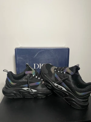 Svarta 22 sneakers - Säljer ett par svarta 22sneakers med chunky sula och meshdetaljer. Skorna har iriserande inslag i lila och grönt, samt tydlig logga på sidan. Snygg och futuristisk design med blandning av läder och textil. Perfekta för dig som gillar statement sneakers.