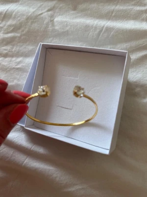 Guldfärgat armband Caroline Svedbom - Snyggt guldfärgat armband från Caroline Svedbom med öppen design och två klara pärlor i varje ände. Perfekt accessoar för att lyfta din outfit med en elegant touch. Kommer i originalask.