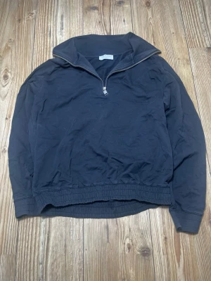 Svart halvzip från Tiger of Sweden - Svart sweatshirt med halv dragkedja från Tiger of Sweden. Tröjan har hög krage, resår i midjan och vid ärmslut samt en stilren design. Perfekt för en avslappnad och snygg look.