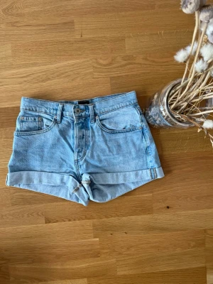 Ljusblå jeansshorts från 157 - Säljer ett par ljusblå jeansshorts från 157 med klassisk femficksdesign och uppvikta benslut. Shortsen har knappgylf och är perfekta för varma dagar. Snygg och enkel stil som passar till det mesta.