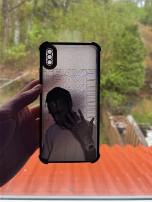Mobilskal Travis Scott motiv svart/vit - Snyggt mobilskal med Travis Scott-motiv i svart och vitt. Skalet har en genomskinlig bakgrund med texten 'TRAVIS' upprepad flera gånger och en bild på artisten. Svarta kanter ger extra skydd och stilren look. Passar perfekt för dig som gillar hiphop och streetwear.