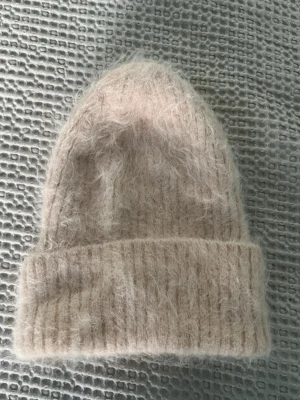 Mössa i alpacka - Mysig och fluffig mössa i ljusbeige från Balmuir. Tillverkad i en lyxig blandning av 78% alpacka, 19% nylon och 3% elastan. Klassisk ribbstickad kant och mjuk, lurvig känsla som håller dig varm under kalla dagar.