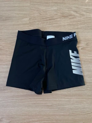 Nike Pro svarta träningsshorts, storlek M - Svarta träningsshorts från Nike Pro med resår i midjan. Stor Nike-logotyp längs ena benet. Kanske en aning små för att vara M. Sparsamt använda.