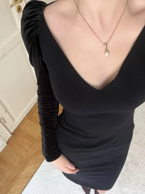 Svart klänning - Snygg svart klänning med v-ringad hals och långa sammet ärmar. Klänningen har en kroppsnära passform och slutar ovanför knäna.