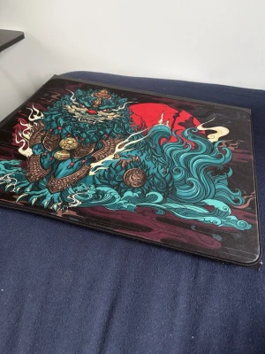 ESPTIGER musmatta med drakmotiv - Säljer en stor musmatta från ESPTIGER med ett färgstarkt drakmotiv i blått, rött och guld. Mattan har en rektangulär form och är tillverkad i tyg med gummibotten för bra grepp. Perfekt för gaming eller datorarbete där du vill ha stil på skrivbordet.