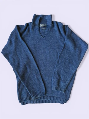 Blå stickad tröja från Polo Ralph Lauren - Snygg blå stickad tröja från Polo Ralph Lauren med hög krage och v-ringning. Tröjan har långa ärmar och ribbade muddar vid ärmslut och nederkant. Perfekt för dig som gillar klassisk och stilren design.