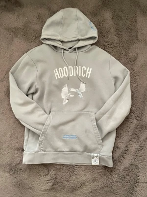  Hoodrich  - Snygg grå hoodie från Hoodrich med vit text och duvor tryckta på både fram- och baksidan. På ryggen står det 'From Nothing To Something' i blått. Stor känguruficka och dragsko i huvan. Perfekt för en chill streetwear-look.