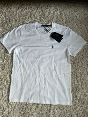 Vit t-shirt från Polo Ralph Lauren - Vit t-shirt från Polo Ralph Lauren i mycket fint skick! Taggen sitter fortfarande kvar, storlek S. Nypris runt 1000kr har jag för mig. Fraktar inom 48 timmar!