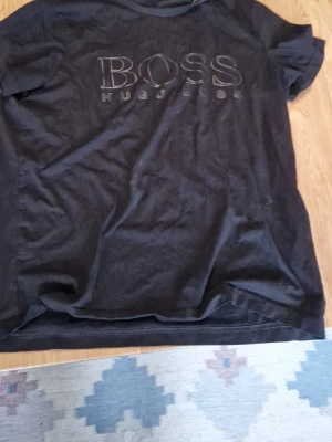 Svart BOSS t-shirt med logga - Snygg svart t-shirt från Hugo Boss med stor BOSS-logga på bröstet. Klassisk passform och rund halsringning. Perfekt till jeans eller shorts för en clean och stilren look.