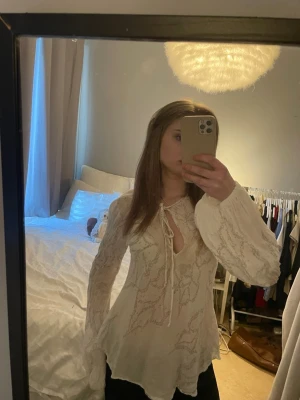 Vit boho-blus med spetsdetaljer - Säljer en vit blus med boho-vibe och vackra spetsdetaljer. Blusen har långa, vida ärmar och knytning vid halsen. Den är lätt transparent och har en flowy passform som ger en avslappnad look. Perfekt för dig som gillar romantiska och trendiga plagg.
