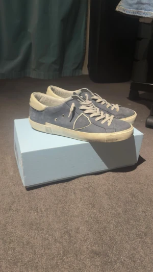 Philippe Model sneakers - Snygga blåa låga sneakers från Philippe Model i mjuk mocka med vita detaljer och vita skosnören. Skorna har en vit sula och den ikoniska sköldloggan på sidan. Perfekta för dig som gillar stilrena och trendiga sneakers. Dem är köpa 2024 från FARFETCH och kvinno finns digitalt. Det finns tecken på användning. Inget slitage och inte så välanvända. Skick: 8,5/10. Pris kan diskuteras vid snabbaffär. Hör av er vid frågor/funderingar!