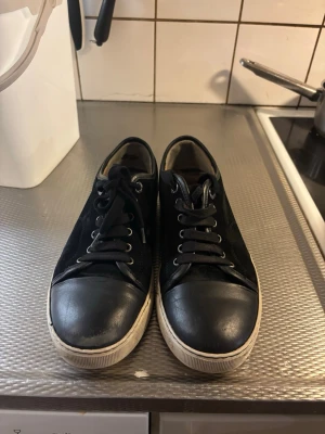 Svarta lanvins - Snygga svarta sneakers med vit sula och tåparti i läderlook. Skorna har svarta skosnören och metallhål för snörningen. Klassisk låg modell som passar till det mesta och ger en clean stil.