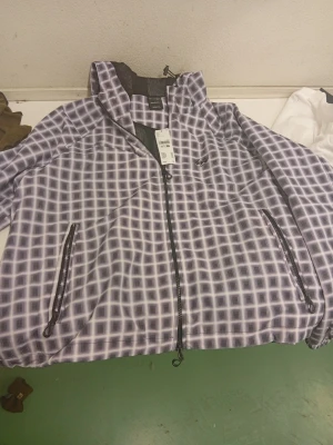 Rutigt vindjacka från Les Deux - Snygg vindjacka från Les Deux med rutigt mönster i svart och vitt. Jackan har dragkedja framtill, två fickor med dragkedja och hög krage. Materialet är lätt och passar perfekt för att skydda mot vind. Logotypen är diskret placerad på bröstet.