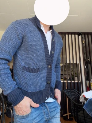 Blå grovstickad kofta med knappar - Snygg blå grovstickad kofta med ribbade muddar och krage. Koftan har två fickor framtill och stängs med fyra knappar. Perfekt att slänga över en t-shirt eller skjorta för en avslappnad look.