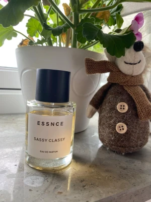 ESSNCE Sassy Classy Eau de Parfum - Fräsch parfym från ESSNCE med namnet Sassy Classy. Flaskan är genomskinlig med en enkel vit etikett och svart lock. Innehållet är ljusgult och flaskan har en stilren, rund form. Perfekt för dig som gillar minimalistisk design. Mängd enl bilder