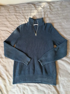 Blå stickad halvzip-tröja från Zara - Märke: ZARA Storlek: M Skick: Bra skick. Färg: Mörkblå Material: 100% bomull Beskrivning: En klassisk och mångsidig mörkblå ribbstickad tröja med hög krage och kvarts dragkedja. Tröjan har en stilren design och är tillverkad i skön och slitstark bomull. Den passar perfekt till både vardag och fest och kan matchas med jeans, chinos eller kostymbyxor. Modellen på bilden är 183 cm lång och väger 72 kg och bär storlek M. 